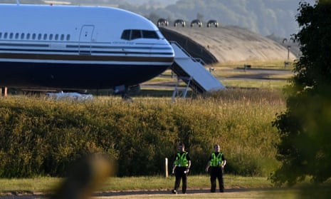 Two police officers walk in grounds near to where a Boeing 767 sits on the runway at the military base in Amesbury, Salisbury, preparing to take a number of asylum seekers to Rwanda.