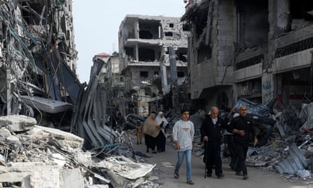 People walk by buildings destroyed in the Israeli bombardment of the Gaza Strip in Nusseirat refugee camp.