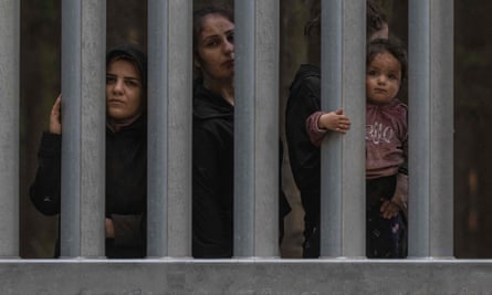 Families from Syria and Iraq wait behind a wall at the Polish-Belarus border