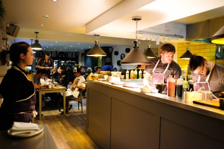 The interior of Skosh restaurant, there are two chefs at the pass and the restaurant beyond is full