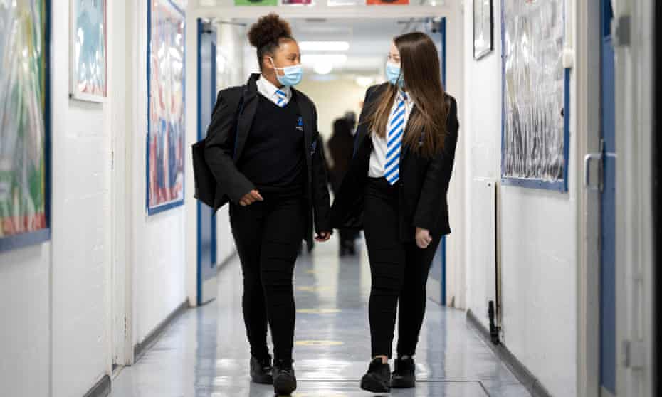 Two girls in uniform wearing masks in a school corridor