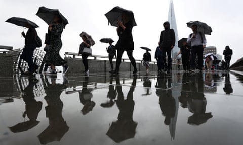 Commuters carry umbrellas while crossing London Bridge