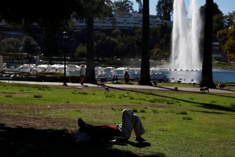 A person lies in a park with a large fountain in a lake in the background.