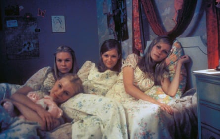 four young, blond-haired girls recline on a bed in light-coloured, floral nighties