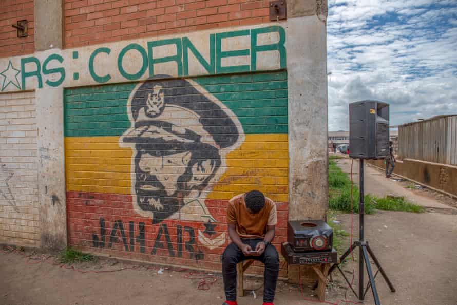A man sits near a mural painted by Basil Matsika.
