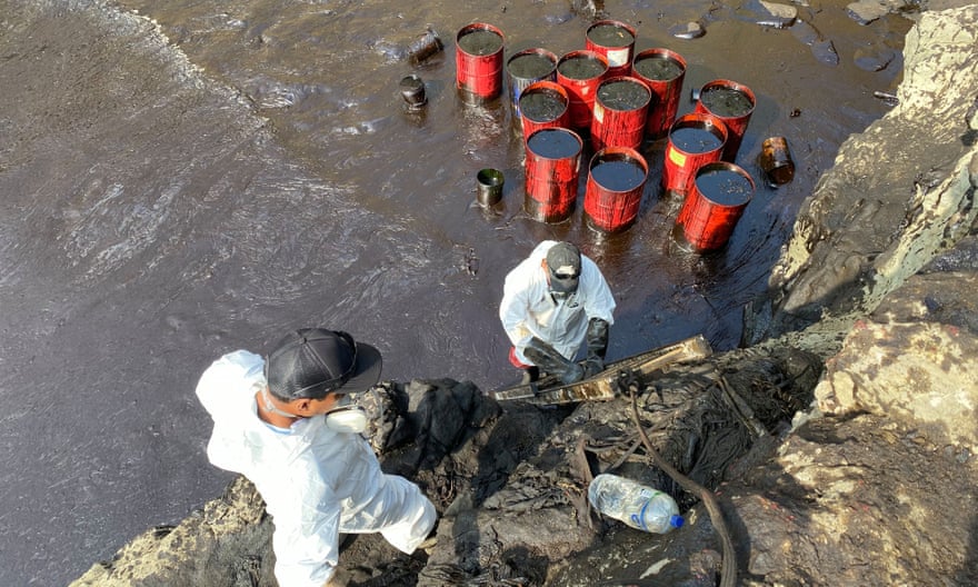 Clean-up workers fill barrels with recovered oil on a beach