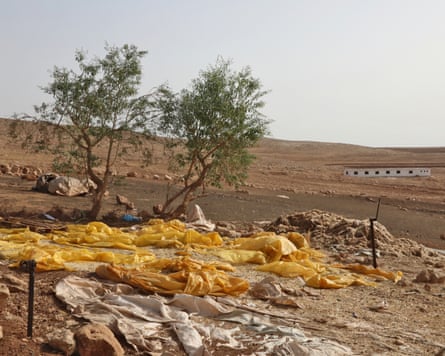 Large pieces of material lie on the ground on a barren hillside with piles of hay nearby