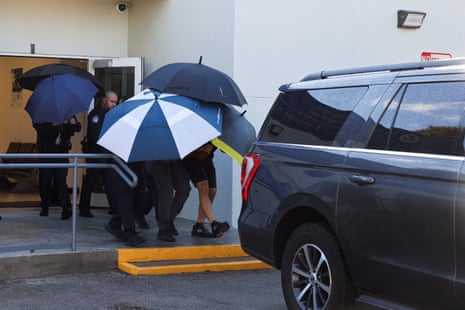 Bolsonaro surrounded by a cluster of open umbrellas, heading for a parked SUV