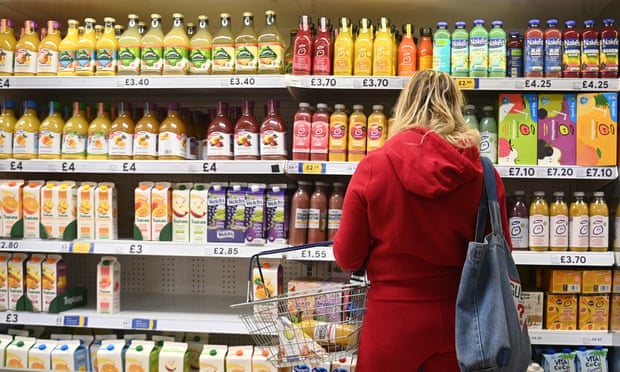 Woman in red holding a shopping basket in front of juice fridge in UK supermarket