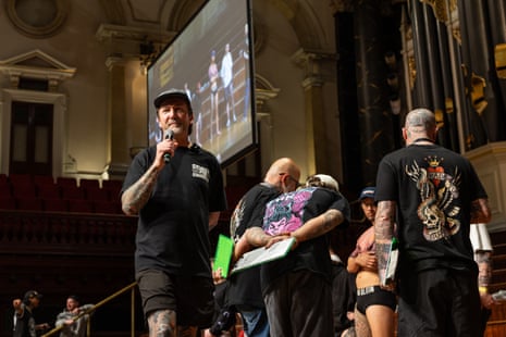 Co-organiser Rhys Gordon stands with a microphone in his hand as the judges for the Best Leg Sleeve competition take notes