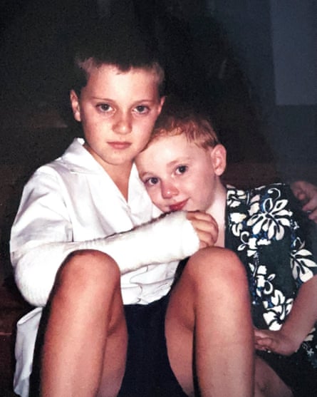 Two young boys sitting on the floor together. The older boy on the left has his arm in a plaster cast. The boy on the right is wearing a flowery black shirt