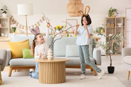 girls in bunny ears decorating tree branches with Easter eggs at home