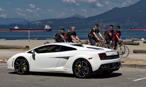 A group of young men look at a Lamborghini sports car stopped in a waterfront park in Vancouver.