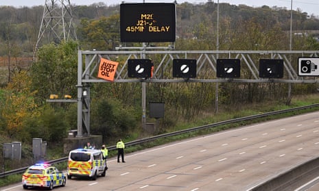 Police officers attempt to stop an activist putting up a banner atop an electronic traffic sign along the M25