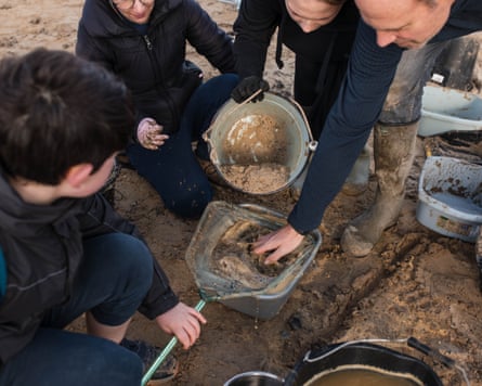 A group of people crouch on the sand around buckets with sieves