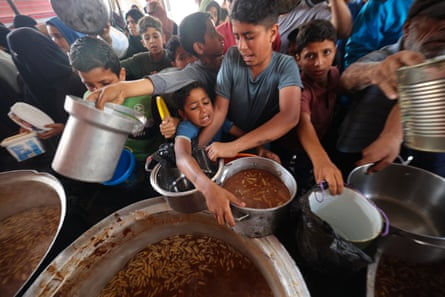 Palestinians crowd around large pots of stew to get bowls filled