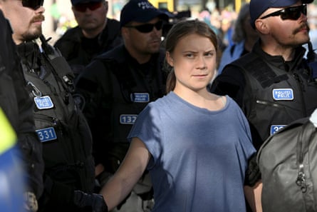 Greta Thunberg, in a T-shirt, looks serious as she is led away from an Extinction Rebellion demonstration by police in Helsinki, Finland