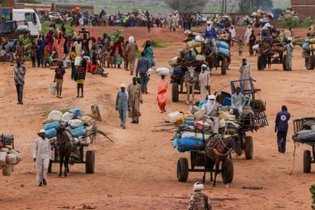 Hundreds of people walking and carrying possessions or on carts pulled by donkeys walk on a red dirt trail
