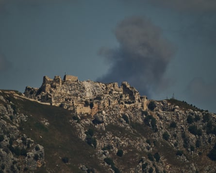 Smoke rises behind a rocky area topped by Beaufort Castle