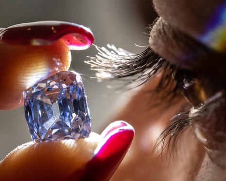 A woman holds up a cut diamond to her eye