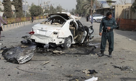 An Afghan police officer investigates a car damaged in a bomb attack in Helmand