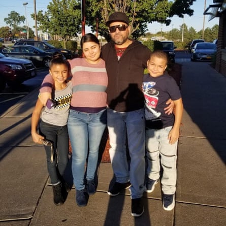 A man with his arms around three children, all smiling into the sun.