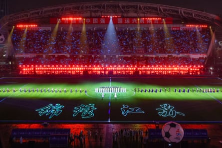 Lights beam on people performing on a field in a stadium at night