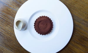 A large round white plate with a chocolate tart in a round, scalloped case in the middle and a small white jug on the edge