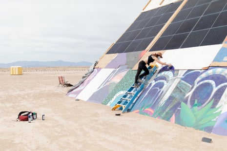 A woman paints a mural on a concrete facade with solar panels