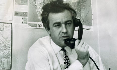 Black and white photo of Godfrey Hodgson on the phone, with maps pinned on the wall behind him