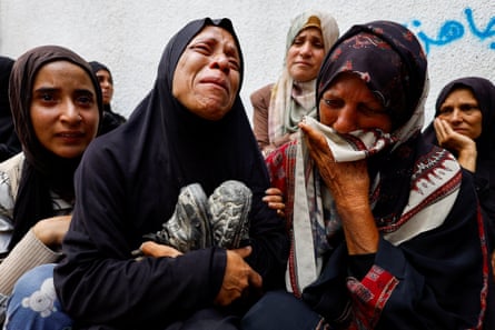 person holds shoes and cries, surrounded by others also mourning