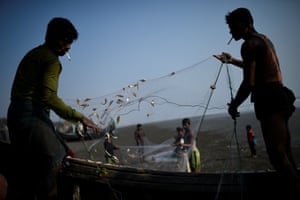 Refugiados Rohingya sacodem peixes recém pescados de redes na praia de Shamlapur