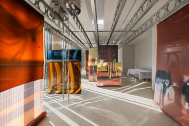Glossy, colourful fabric panels hang in a gallery with metal ceiling fixtures and tiled floor