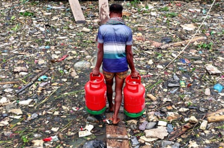 A man walks across a bridge on the Karnaphuli River in Chattogram, Bangladesh, which is full of plastic waste