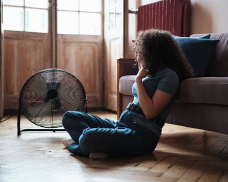 Summer heat. Young woman sitting on floor near electrical fan at home, cooling down during heatwave indoors