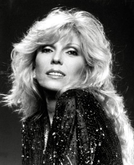 ترتدي قميصًا أسود لامع، وتنظر إلى الوراء نحو الكاميرا، مبتسمة