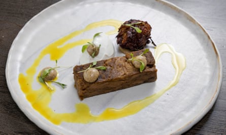 Rectangle of curried salted lamb with bhaji and yellow drizzle on white round plate
