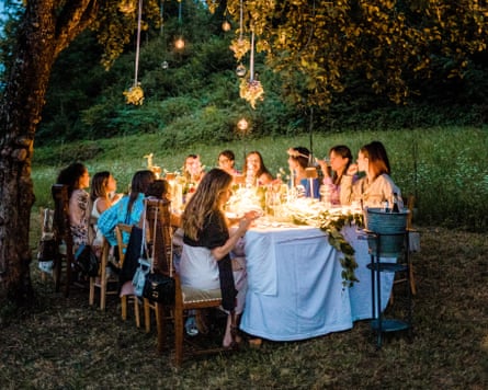 A group of young woman eating at a table with a white tablecloth outdoors under a tree in the evening.