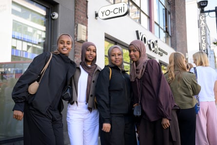 Four young women in headscarves smile and pose in front of a restaurant.