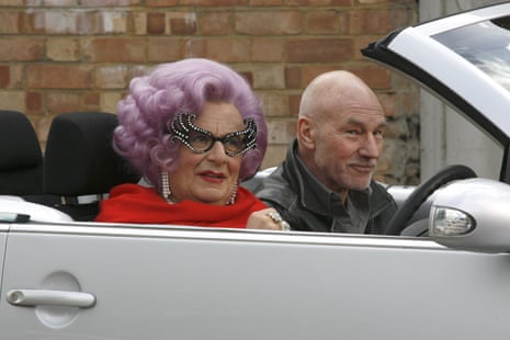 Dame Edna Everage, in a purple wig, rides with Sir Patrick Stewart in a convertible