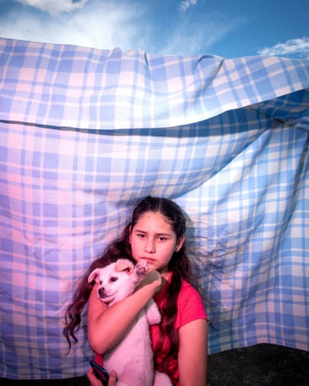 A girl holds a small dog in her arms. She is standing in front of a checked sheet on a washing line, with blue sky above.