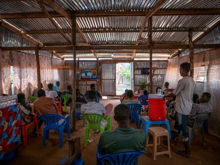 Men sit on plastic chairs watching TV in the Giddu Adam Eissa cafe in Gorom