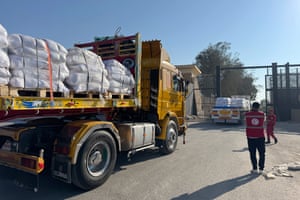 Members of Egyptian Red Cross stand by a truck loaded with aid, as another truck passes through a border gate in the background