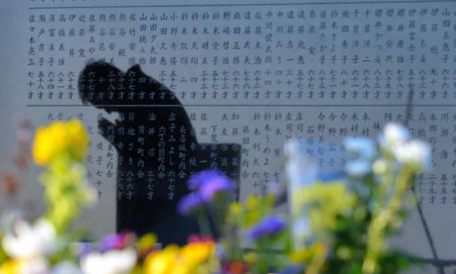 a man prays in Sendai, Miyagi, Japan, reflected on a stone memorial commemorating the 2011 tsunami.