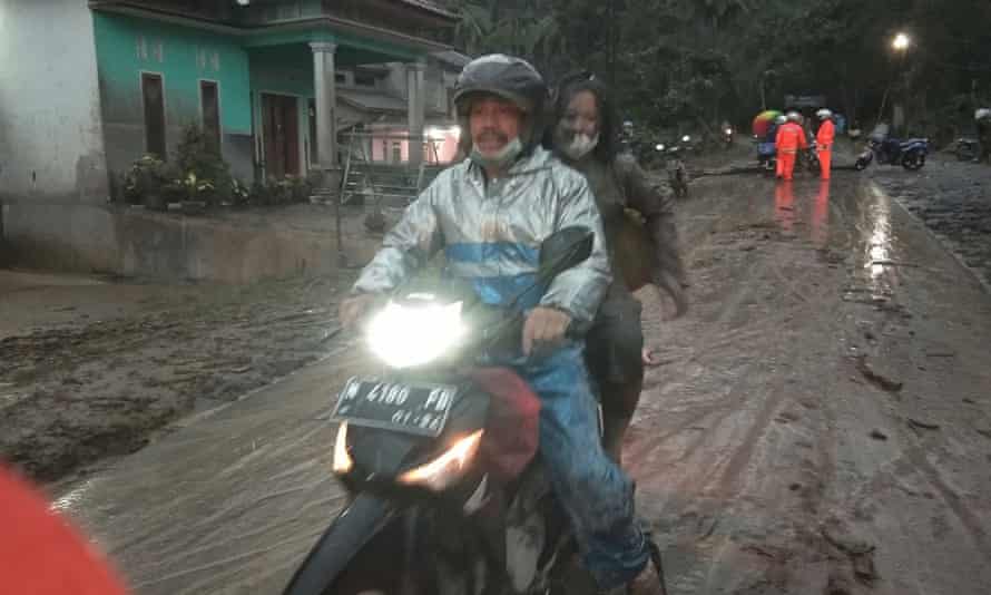 People ride a motorbike on a road that is covered with volcanic ash following an eruption of the Semeru mount volcano.