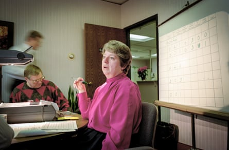 A woman in a pink blouse and a man in a patterned jumper sitting at desks in an office