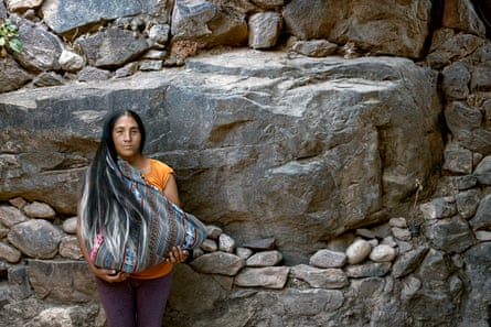 An Indigenous woman in front of a rock face with her baby held in a traditional woven shawl