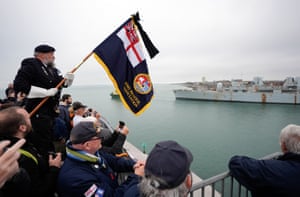A standard bearer amid a crowd watches a vessel