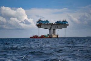 A floating red pontoon or barge can be seen under a section of a large concrete bridge in the sea