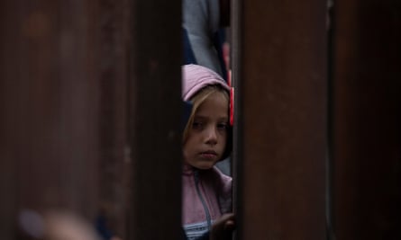 Small blond girl looks through rusty bars of wall.